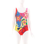Woman wearing a colorful abstract one piece swimsuit by Gottex.Red, blue, yellow, pink and green colors. Heart, chain, rope pattern. Full rear coverage, standard shoulder straps.
